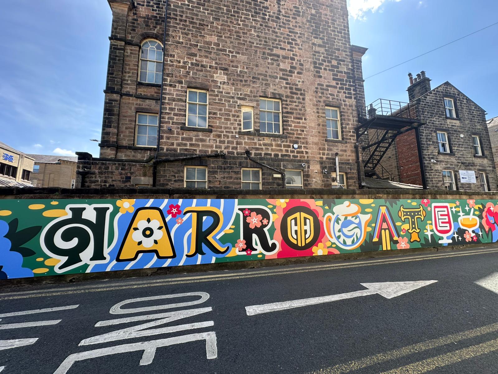 Colorful mural on a building wall with text and graphics, set against a clear blue sky.
